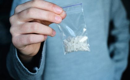 A man in a blue shirt holding a plastic bag containing white crystals. 